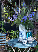 Blue table in the garden with tea service and blue and white vase with delphinium