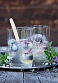 Two glasses of herbal lemonade with ice and edible flowers on a rustic wooden table