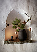 Wall niche with decorative fir branch in vase and candlelight