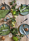 Wooden table set with crockery, napkins and flower arrangement in shades of green