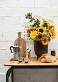 Wooden table with a bouquet of sunflowers in a black vase, espresso maker and cups