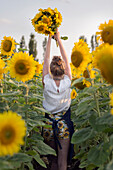 Frau hält Blumenstrauß aus Sonnenblumen (Helianthus) im Sonnenblumenfeld hoch