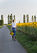 Woman with bouquet of sunflowers on rural road next to sunflower field