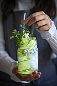 Woman holding flavoured water with cucumber, lime and edible flowers