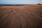 Ein Paar geht am Strand spazieren, während ein starker Wind den Sand wegbläst, auf Lanzarote, Kanarische Inseln, Spanien