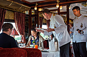 Ein Kellner serviert das Mittagessen im Art-Deco-Restaurantwagen des Luxuszuges Belmond Venice Simplon Orient Express. Lachskraut und Kartoffeln