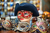 Verschnörkelte Karnevalsmaske zwischen bunten Federn in Venedig, Italien. Eine Ausstellung von Maskenballmasken und venezianischen Masken in Bardolino am Gardasee in der Region Venetien, Italien