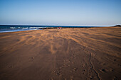 Ein Paar geht am Strand spazieren, während ein starker Wind den Sand verweht, Lanzarote, Kanarische Inseln, Spanien