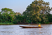 Kleines Holzboot mit Einheimischen auf dem Purus-Fluss im Amazonasgebiet an einem sonnigen Sommertag mit Bäumen am Flussufer, in der Nähe von Iquitos, Loreto, Peru. Fahrt auf einem der Nebenflüsse des Amazonas nach Iquitos, etwa 40 Kilometer von der Stadt Indiana entfernt