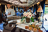 A waiter serves wine inside the art deco bar lounge wagon of the train Belmond Venice Simplon Orient Express luxury train.