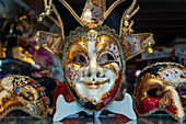 Verschnörkelte Karnevalsmaske zwischen bunten Federn in Venedig, Italien. Eine Ausstellung von Maskenballmasken und venezianischen Masken in Bardolino am Gardasee in der Region Venetien Italien