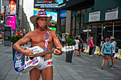 Robert Burck, besser bekannt als der Nackte Cowboy, tritt in der Abenddämmerung auf dem Times Square auf. Manhattan, New York City, USA