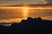 Eine Sonnensäule bei Sonnenaufgang über den Bergen, verursacht durch Licht, das von Eiskristallen in der Atmosphäre reflektiert wird. Quartzsite, Arizona