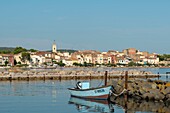 France, Herault, Bouzigues, boat moored on a dike with a village and its bell tower in the background