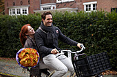 Couple riding bicycle holding flowers