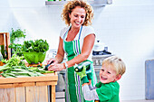 Woman cutting green vegetables and salad with her son, kitchen