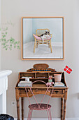 Old wooden desk with pink metal chair and painting of cat on the wall