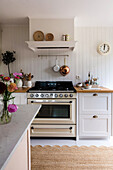 Kitchen with white gas hob, copper pans and flowers on white worktop