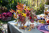 Herbstlicher Blumenstrauß aus Sonnenbraut (Helenium) und Farn auf gedecktem Gartentisch