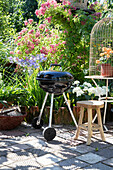 Kettle barbecue in flowering garden next to rustic stool and birdcage