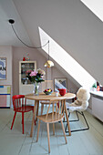 Dining area under a sloping roof with wooden and metal chairs, bouquet of flowers and fruit bowl