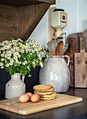 Fresh chamomile in vase and pastries with eggs on wooden board in kitchen