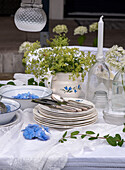 Laid garden table with porcelain plates, flowers and white lace tablecloths