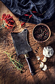 Old butcher's cleaver on a chopping board, surrounded by chilli peppers, garlic and rosemary