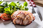 Fried Brie cheese wrapped in bacon with cherry tomatoes and leaf salad