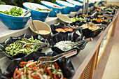 Salads and fresh vegetables in bowls on buffet table in hotel
