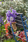 Bergaster (Aster amellus) und Dahlie (Dahlia) als Blumenstrauß in kleinem Flacon hängend an Gartenstuhl