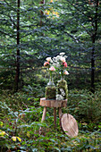 Glass bottles wrapped in moss with roses and gypsophila on a rustic wooden table in the forest