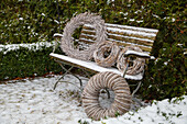 Snow-covered garden bench with decorative wreaths in winter