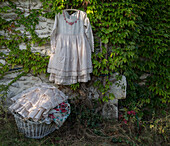 White vintage dress on an overgrown stone wall, woven laundry basket next to it