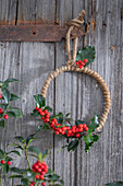 Winterkranz mit Roter Winterbeere (Ilex verticillata), Stechpalme 'Blue Maid' (Ilex meserveae) an Holzwand