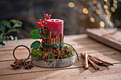 Candle on birch disc with cinnamon sticks wrapped with red winter berries, holly, star anise and moss, Advent arrangement