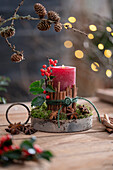 Candle on birch disc with cinnamon sticks wrapped with red winter berries, holly, star anise and moss, Advent arrangement
