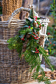 Advent arrangement with fir branch of hemlock, holly (Ilex meserveae) 'Blue Maid' and cones on wicker basket