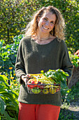 Woman holding basket with harvest chard &#39;Bright Lights&#39;, wax bean &#39;Neckargold&#39; and different kinds of tomatoes