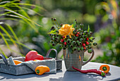 Strauß mit Rose (Rosa), Hagebutten (Rosa canina) in grün und rot und Paprika auf Tablett
