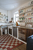 Country-style kitchen with open shelves and red and white tiled floor, cat sitting on worktop