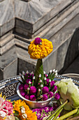A votive offering at the base of of a statue in the Temple of the Emerald Buddha complex, Grand Palace, Bangkok, Thailand.