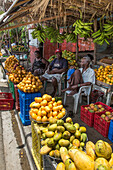 Drei Personen verkaufen Mangos an einem Obststand am Straßenrand in Bani, Dominikanische Republik