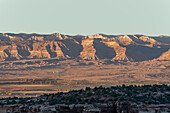 Die Book Cliffs und Farmen im Grand Valley bei Fruita, Colorado, bei Sonnenuntergang. Links in der Mitte befindet sich eine kleine Erdölraffinerie