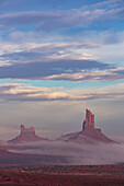 Foggy morning North Window view of the Utah monuments in the Monument Valley Navajo Tribal Park in Arizona. L-R: Setting Hen, Big Indian Chief.