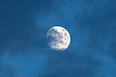 A waxing gibbous moon with clouds photographed in the daytime with a telephoto lens over New Mexico.