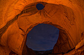 Stas & clouds through the Big Hogan Arch at night in the Monument Valley Navajo Tribal Park in Arizona.