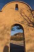 Arched doorway through the protective wall around the Mission San Xavier del Bac frames the Grotto Hill, Tucson Arizona.