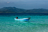 Ein Motorboot liegt im klaren, flachen Wasser um Cayo Arena oder Paradise Island vor Anker. Im Hintergrund ist der Nationalpark Monte Cristi in der Dominikanischen Republik, Hispaniola, zu sehen.