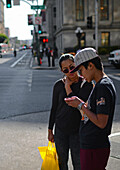 Two people checking smartphone in street, San Francisco.